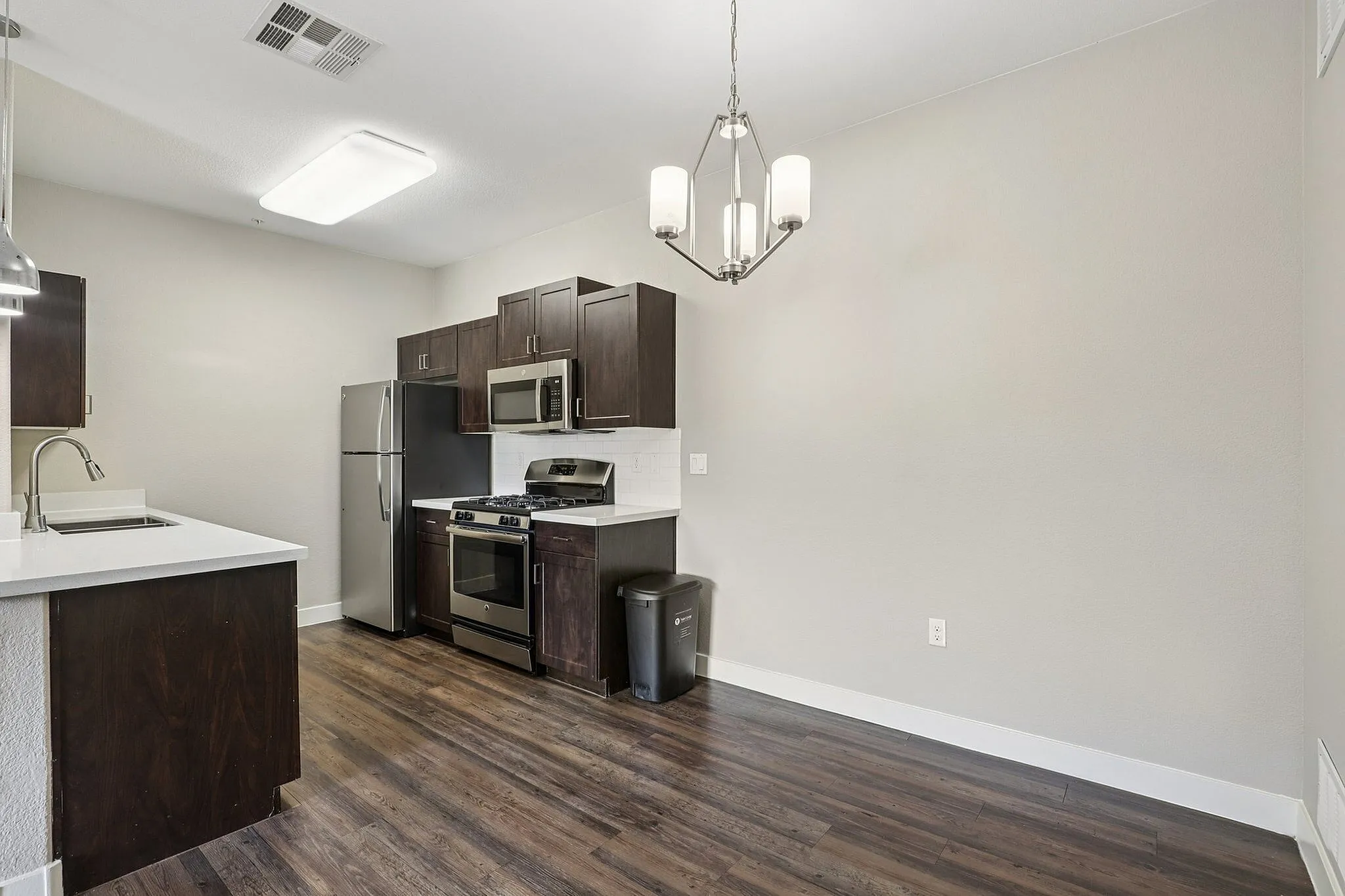 Sleek, modern kitchen with stainless steel appliances, elegant dark cabinetry, and a chic light fixture, offering a stylish and functional space.