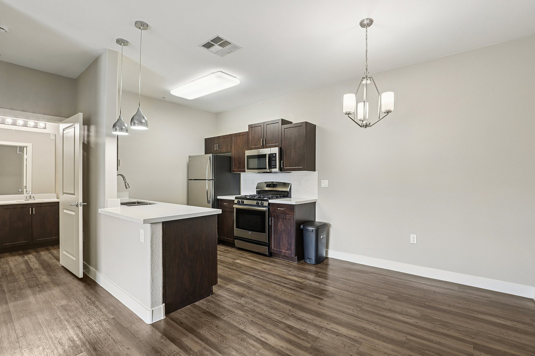 Modern kitchen with stainless steel appliances, elegant wood cabinetry, and chic pendant lighting over a sleek island, complemented by stylish hardwood floors.