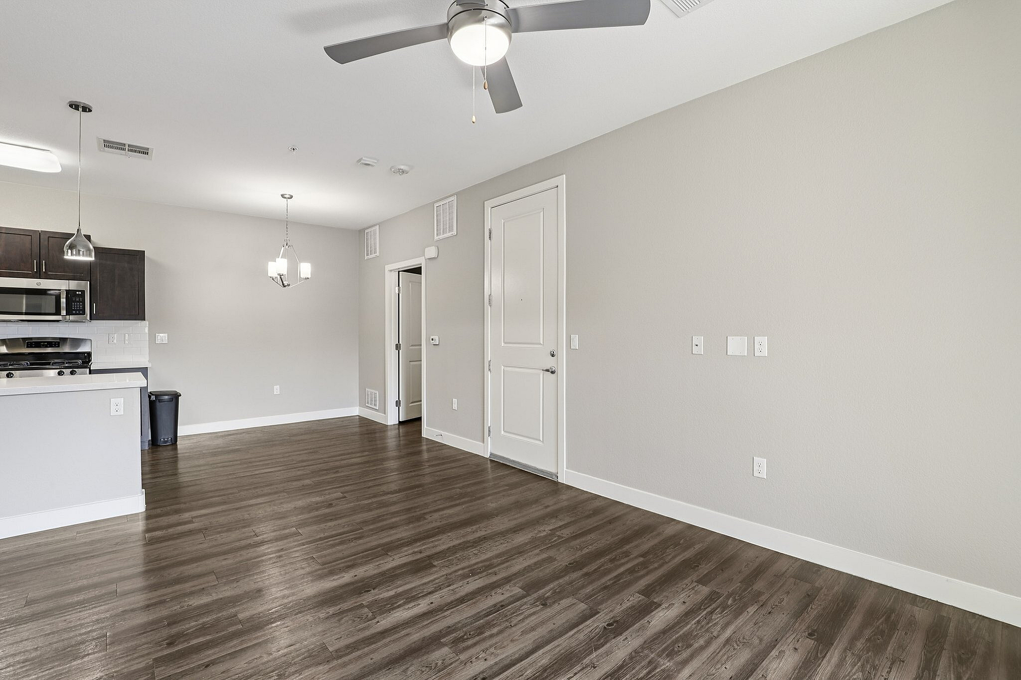 Bright and modern open-concept living area featuring sleek hardwood floors, stainless steel kitchen appliances, and elegant pendant lighting.