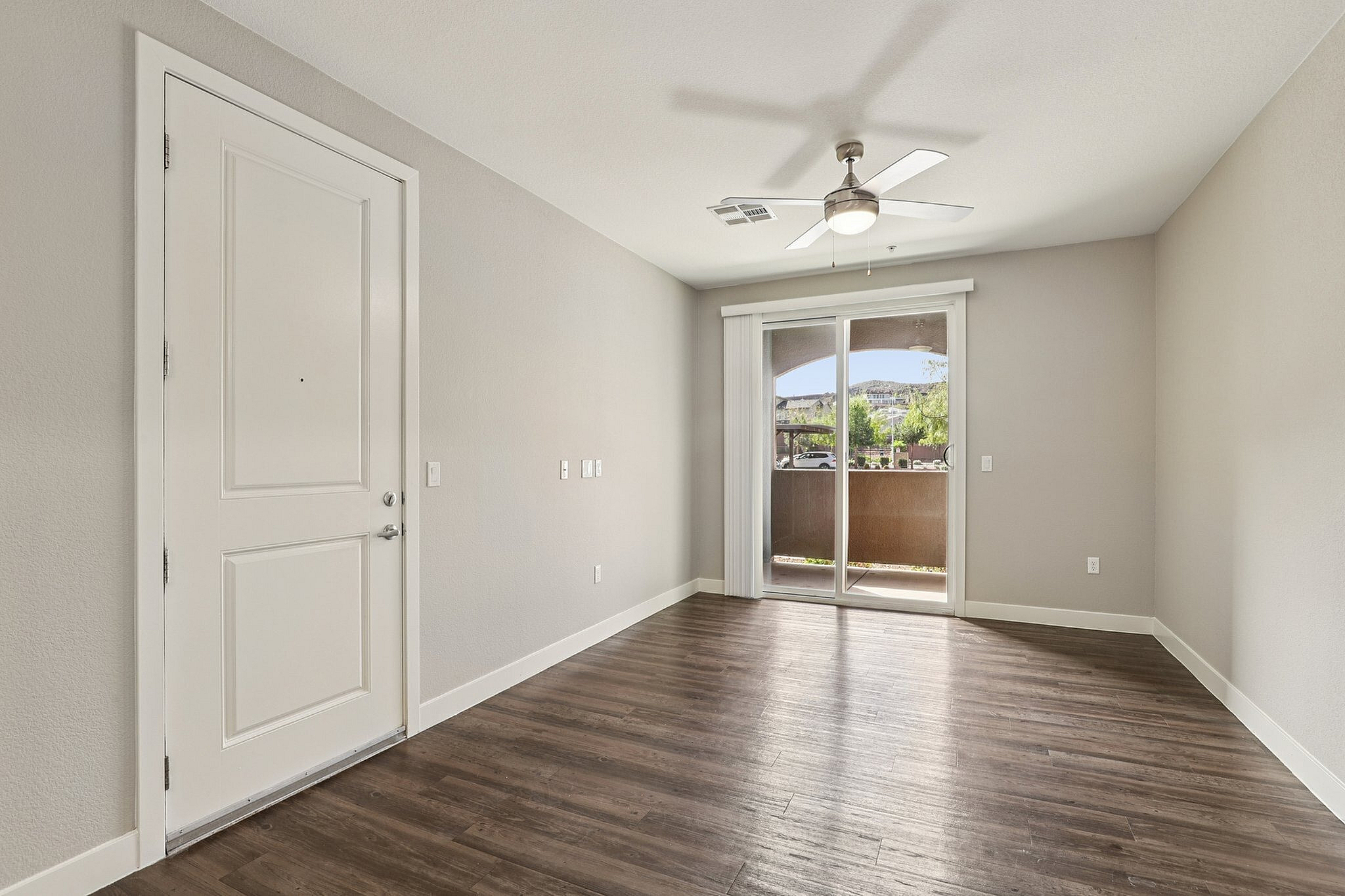 Bright and airy modern room featuring sleek wooden flooring, large sliding glass door, and ceiling fan, providing a welcoming entry space.