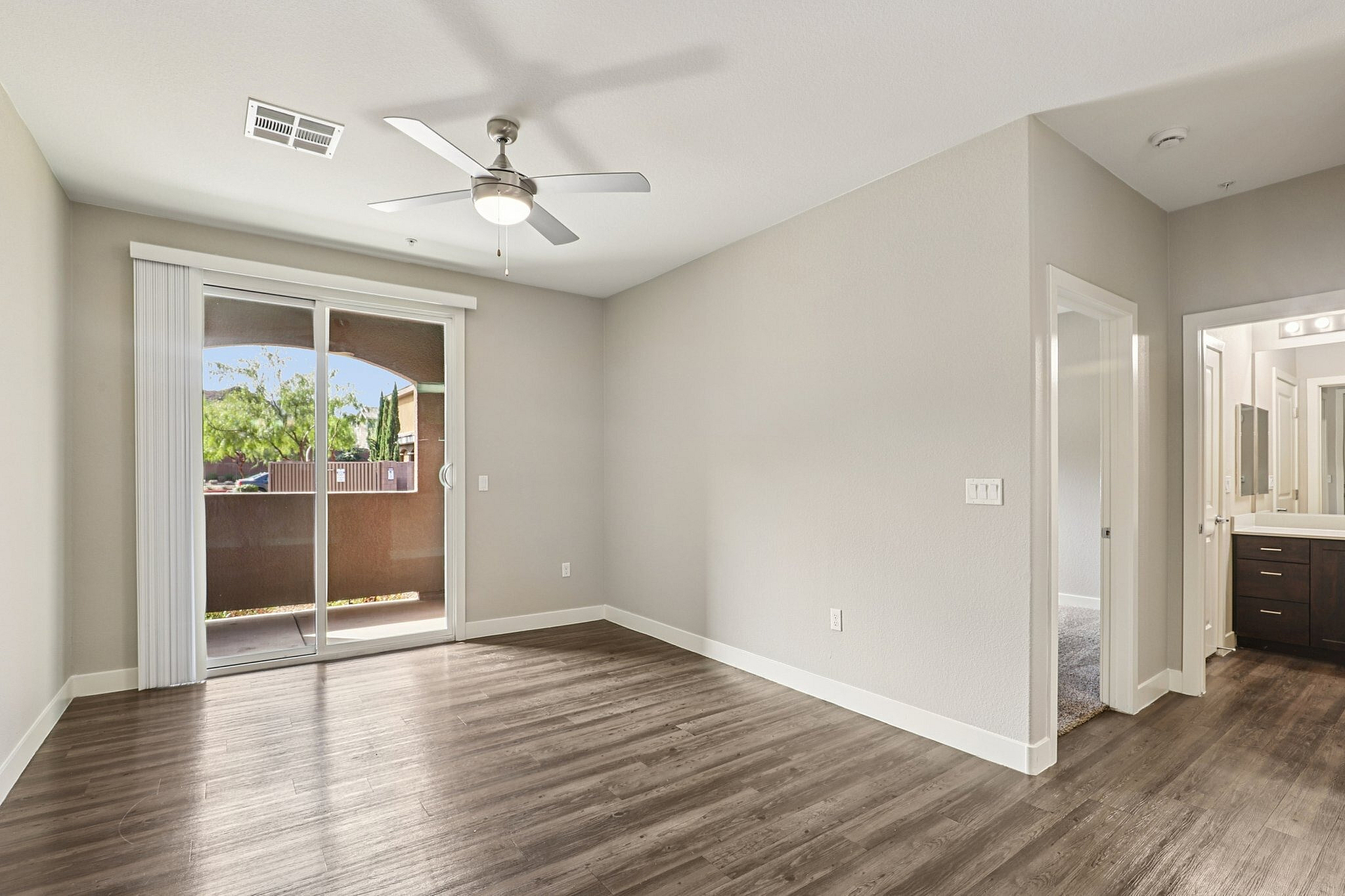 Bright and airy apartment interior featuring sleek hardwood floors, large sliding glass doors leading to a balcony, and modern ceiling fan.