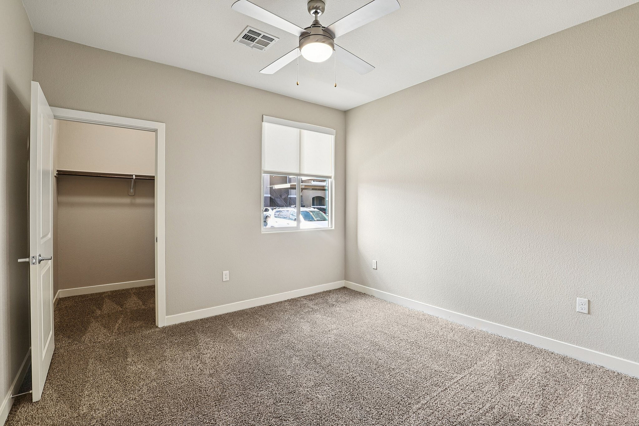 Bright, spacious bedroom with plush carpet, ceiling fan, walk-in closet, and natural light streaming through the window.