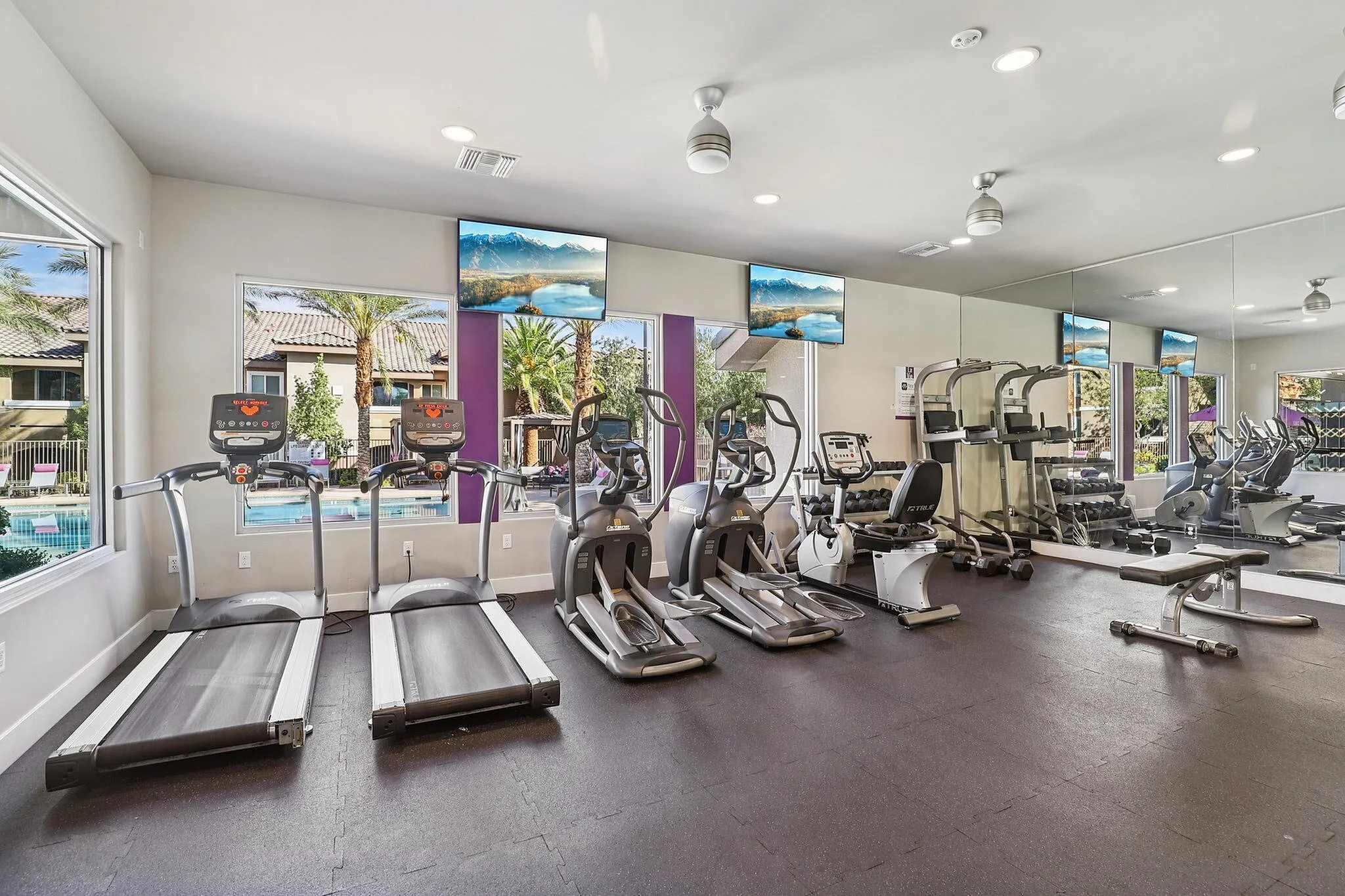 Modern fitness center featuring state-of-the-art cardio equipment, bright and airy space with large windows overlooking a scenic outdoor pool.