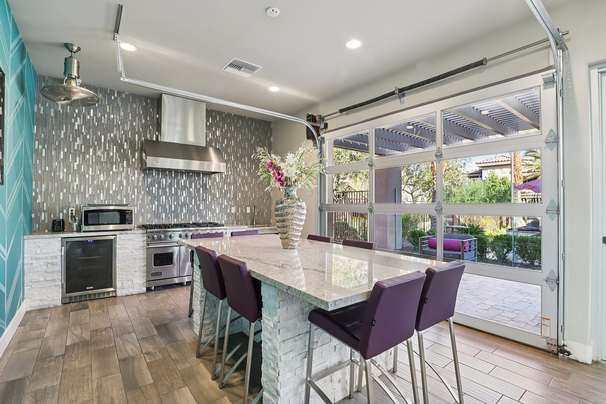 Modern kitchen with stylish backsplash, large marble island, purple chairs, and glass doors opening to a garden view.