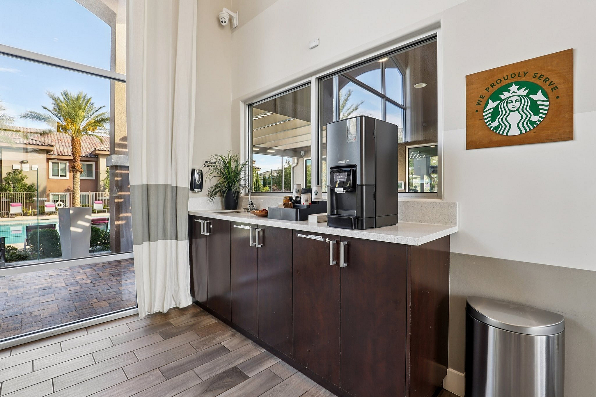 Inviting apartment coffee corner with modern espresso machine, showcasing a lush poolside view under sunny skies.