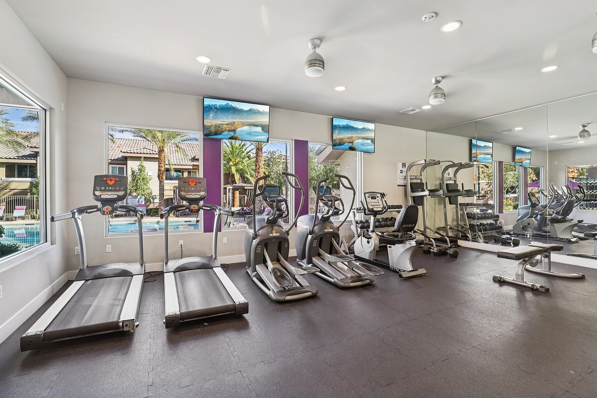 Modern fitness center with state-of-the-art equipment, including treadmills and elliptical machines, boasting floor-to-ceiling windows with pool views.