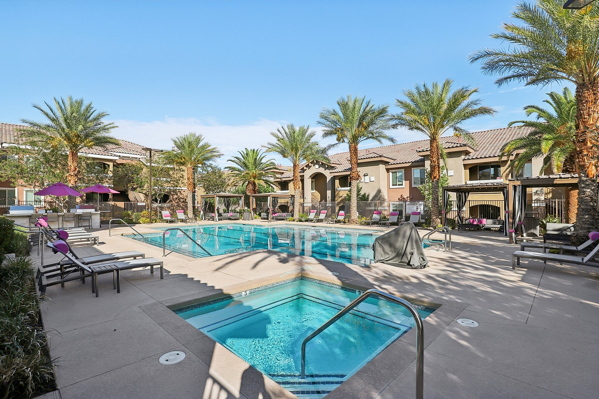 Luxurious apartment complex featuring a sparkling swimming pool and stylish lounge chairs under palm trees for a resort-style living experience.