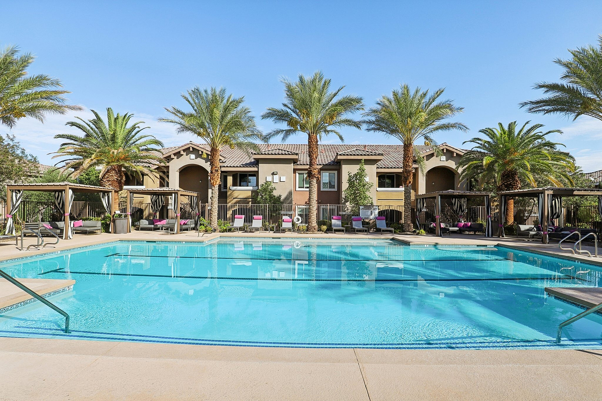Luxurious apartment complex featuring a sparkling pool surrounded by elegant cabanas and lush palm trees, offering a resort-style living experience.