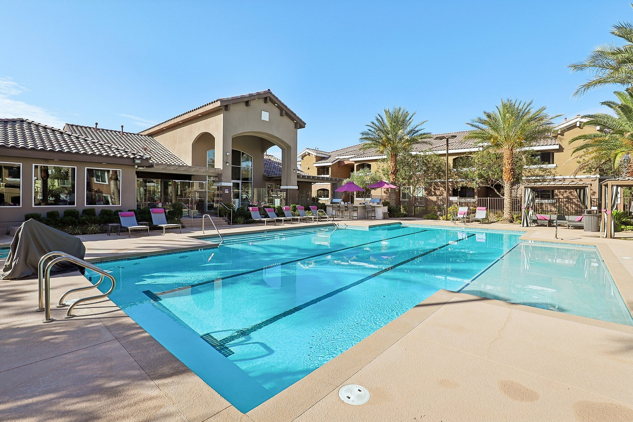 Luxurious apartment complex featuring a sparkling swimming pool, surrounded by elegant palm trees and shaded lounging areas.