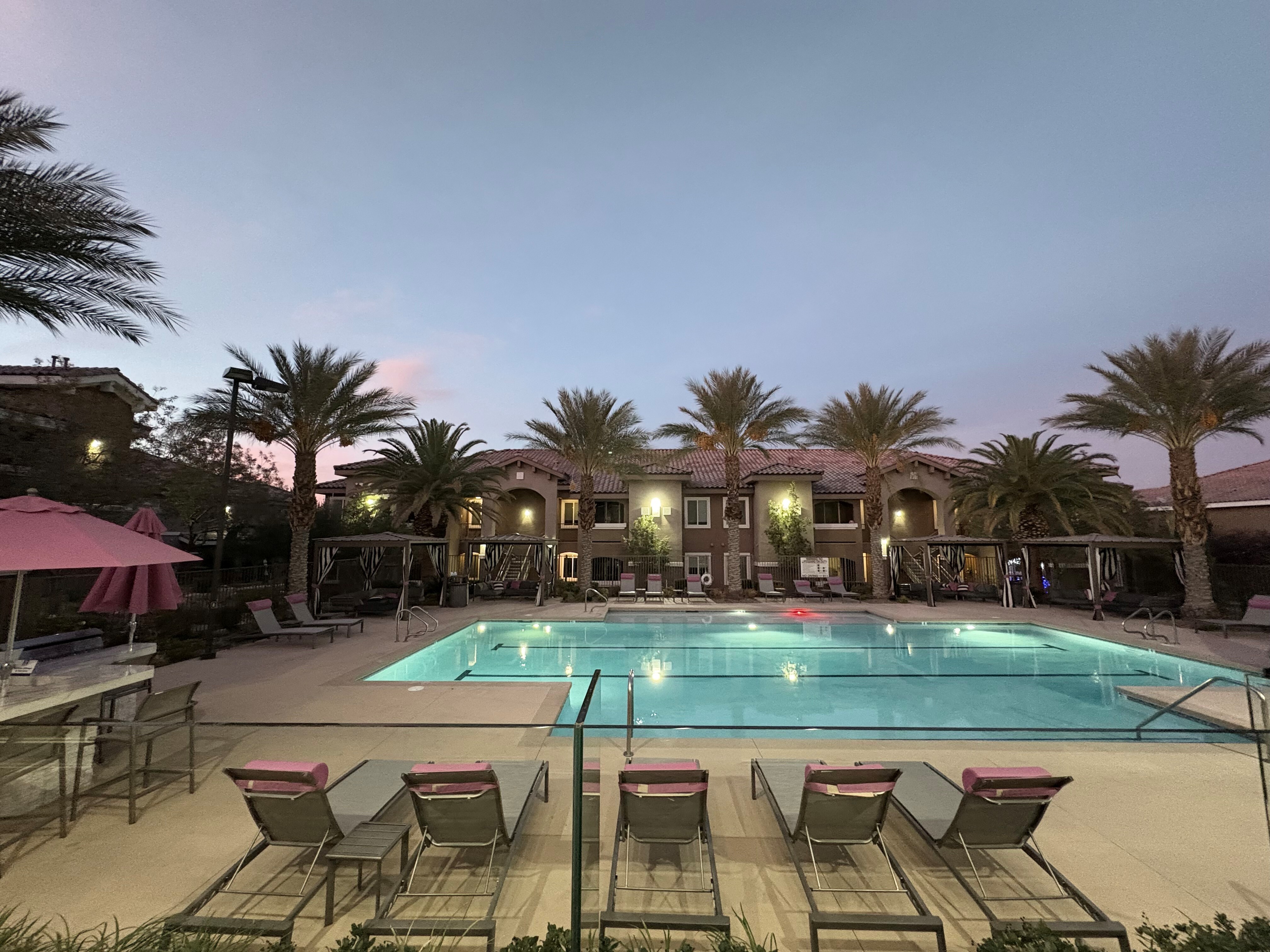 Luxurious apartment complex with a stunning outdoor pool, surrounded by palm trees and cozy loungers, perfect for sunset relaxation.