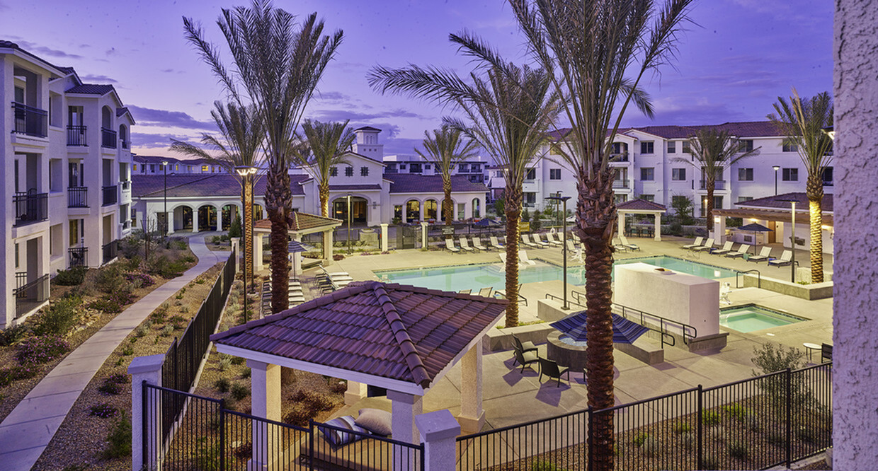 Enchanting twilight view of a luxurious apartment community featuring a sparkling pool, cozy seating areas, and lush palm trees, promising a serene lifestyle.