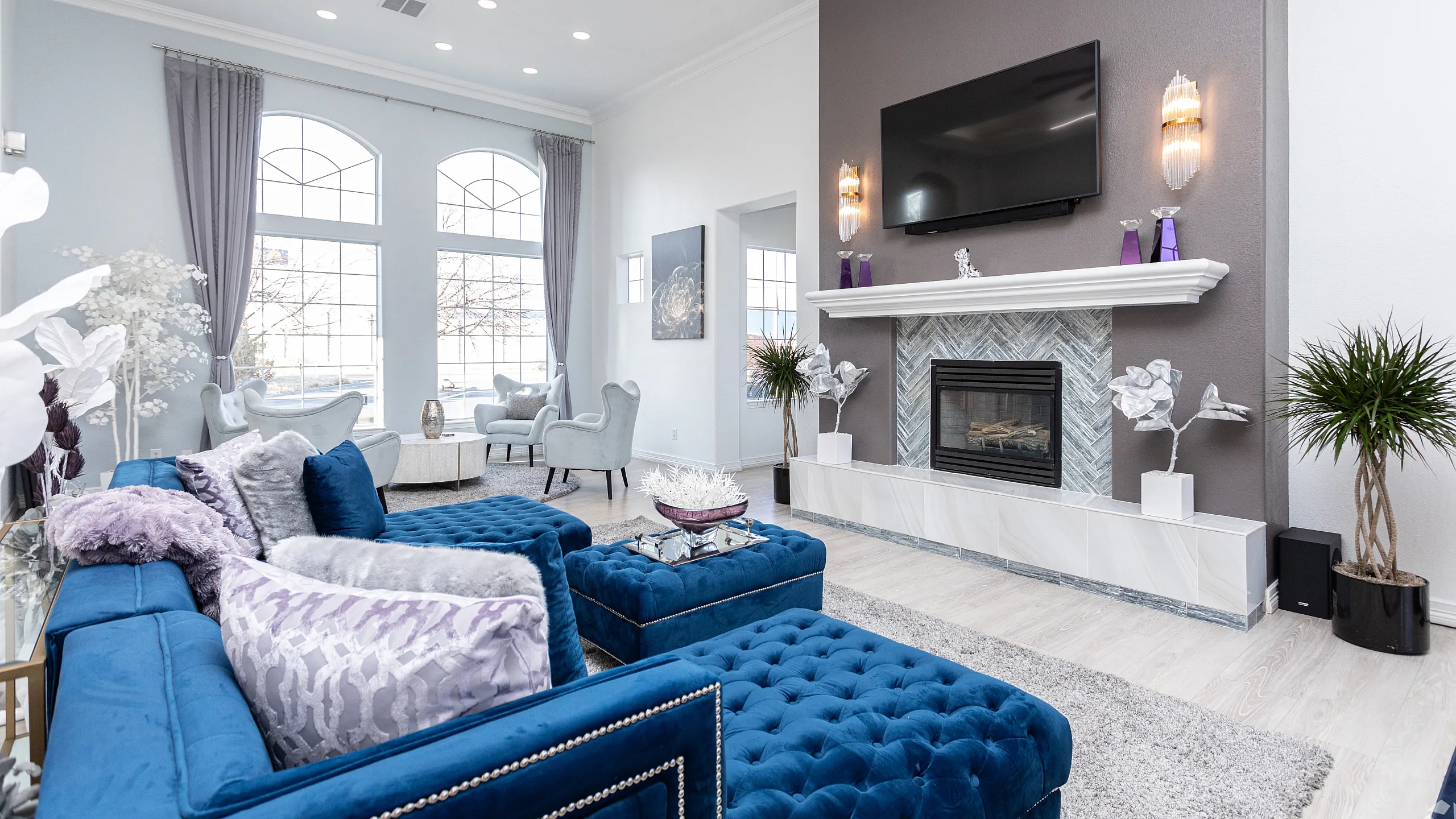 Bright and elegant living room featuring plush blue seating, a stylish fireplace, and large windows with flowing curtains.