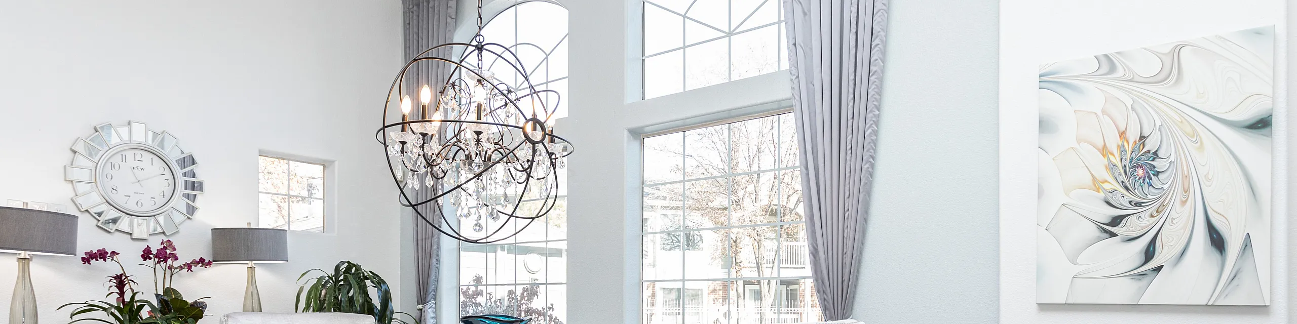Luxurious dining space featuring plush gray chairs, ornate chandelier, and large arched windows.