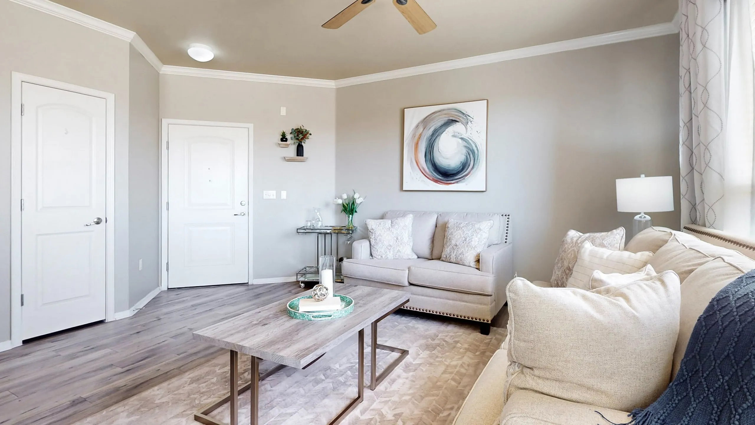 Stylish living room with plush sofas, modern art, and a ceiling fan, offering a warm ambiance.