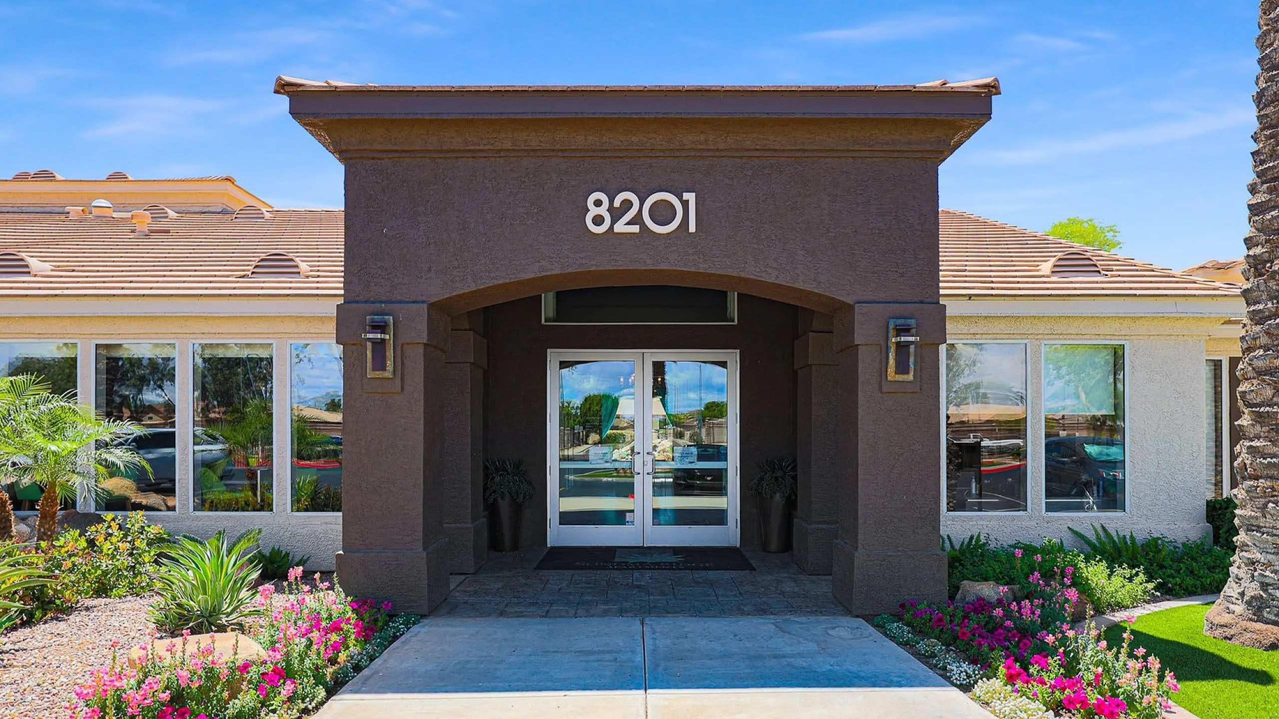 Charming entrance of a modern apartment building surrounded by lush landscaping and vibrant flowers, showcasing elegance and curb appeal.
