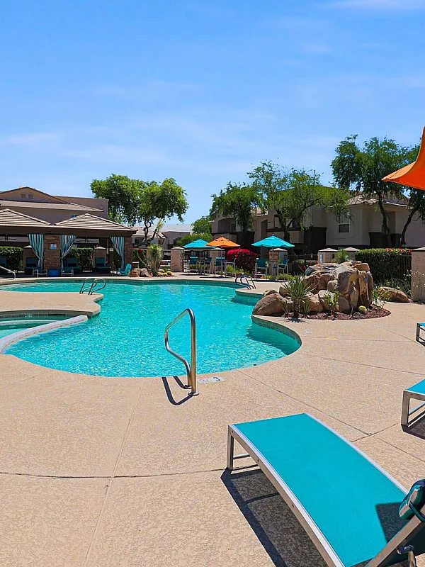 Inviting swimming pool area with vibrant sun loungers, a resort-style cabana, and colorful umbrellas under a clear blue sky.
