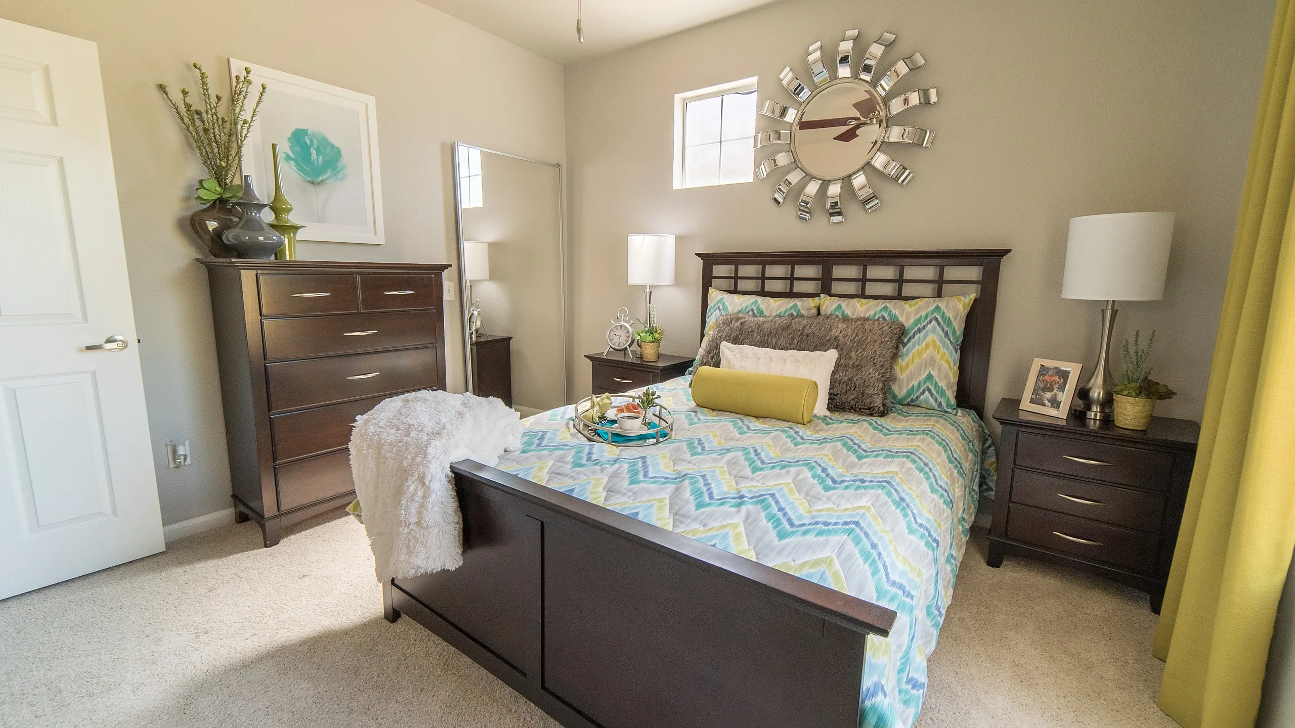 Inviting bedroom with chic decor, featuring a comfortable bed, elegant dresser, and stylish wall art complemented by natural light.