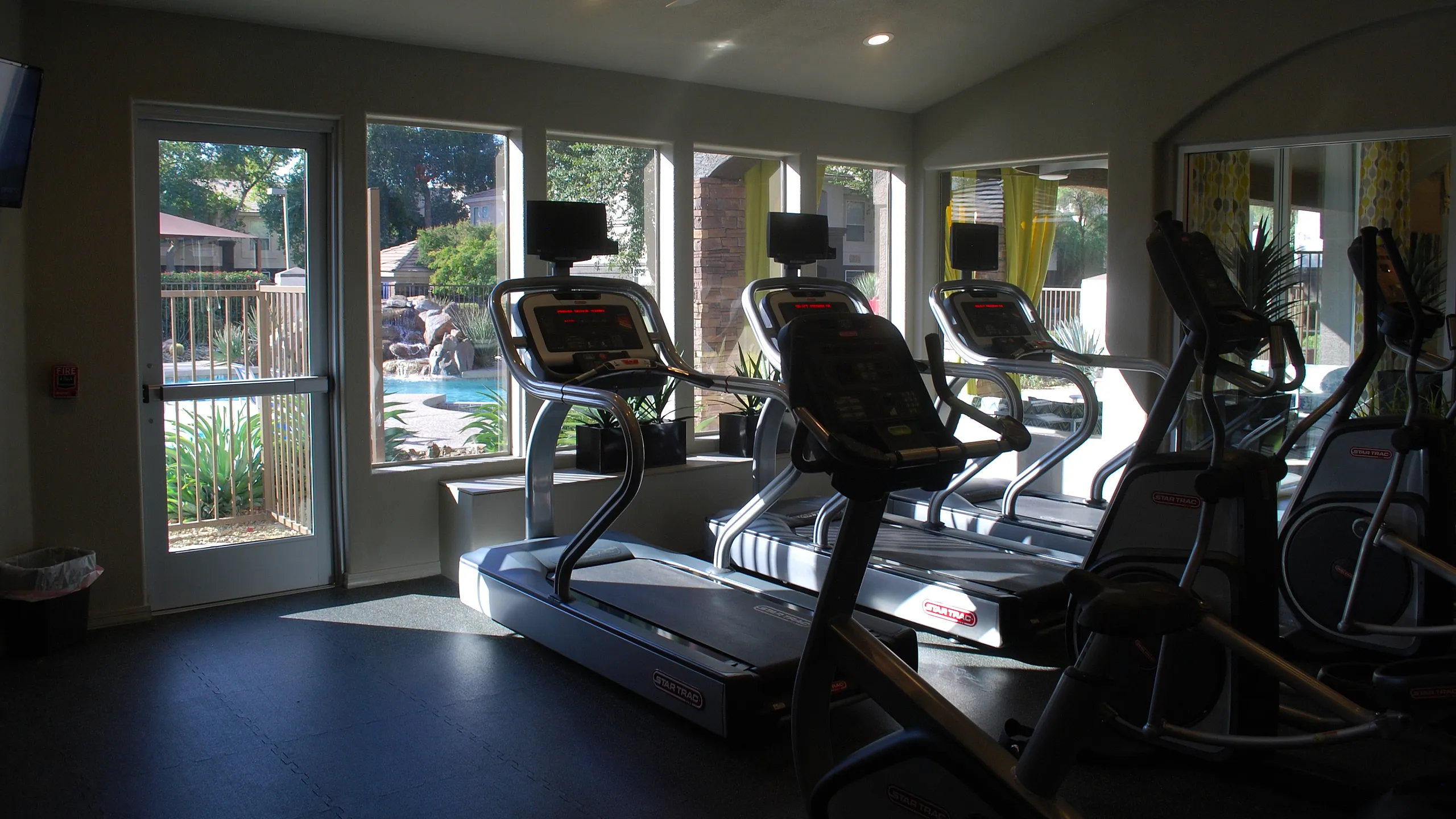 Modern fitness center with state-of-the-art treadmills, overlooking a refreshing outdoor pool area through large windows.