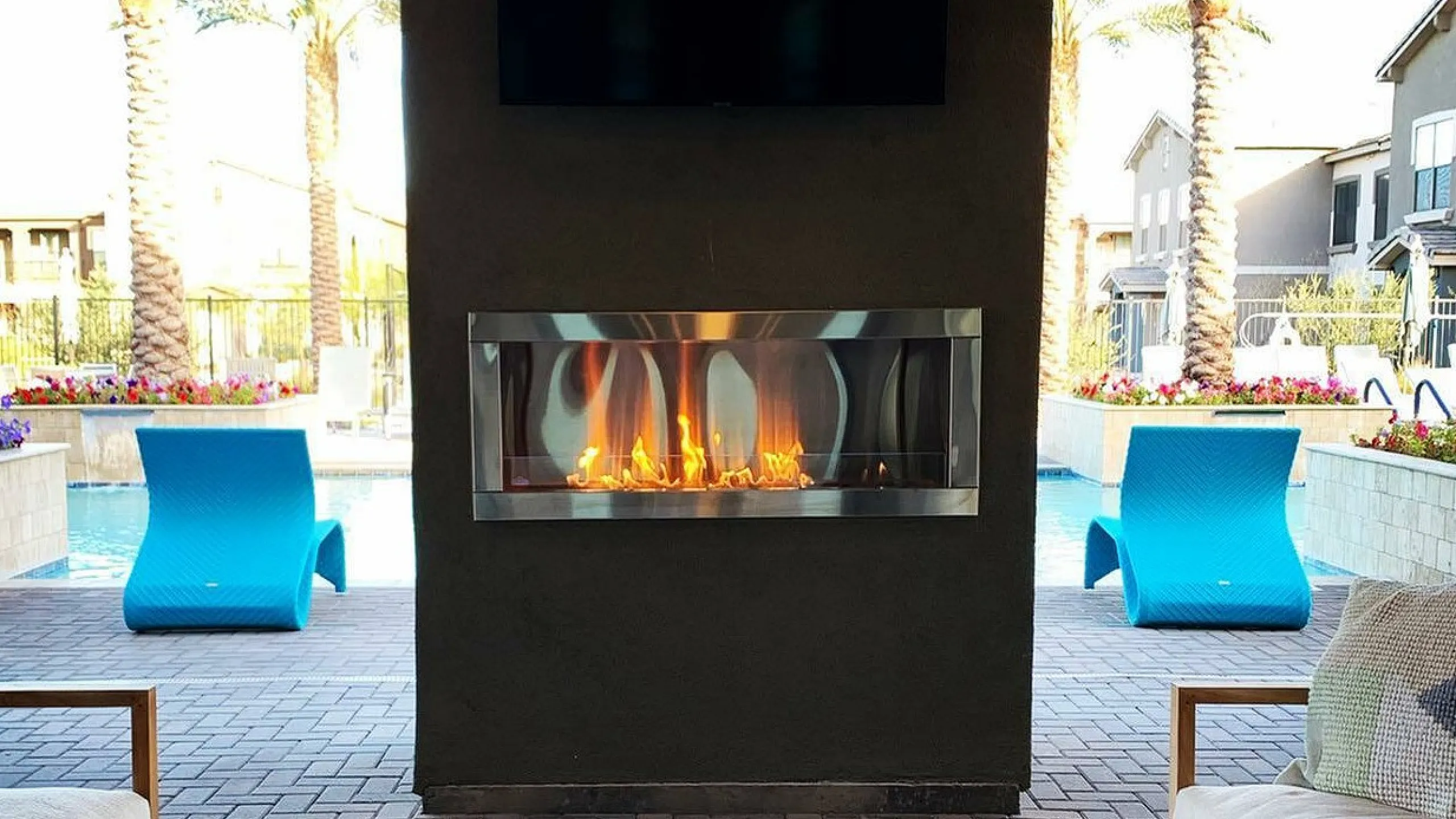 Luxurious outdoor lounge with cozy seating, modern fireplace, and inviting poolside view under palm trees.