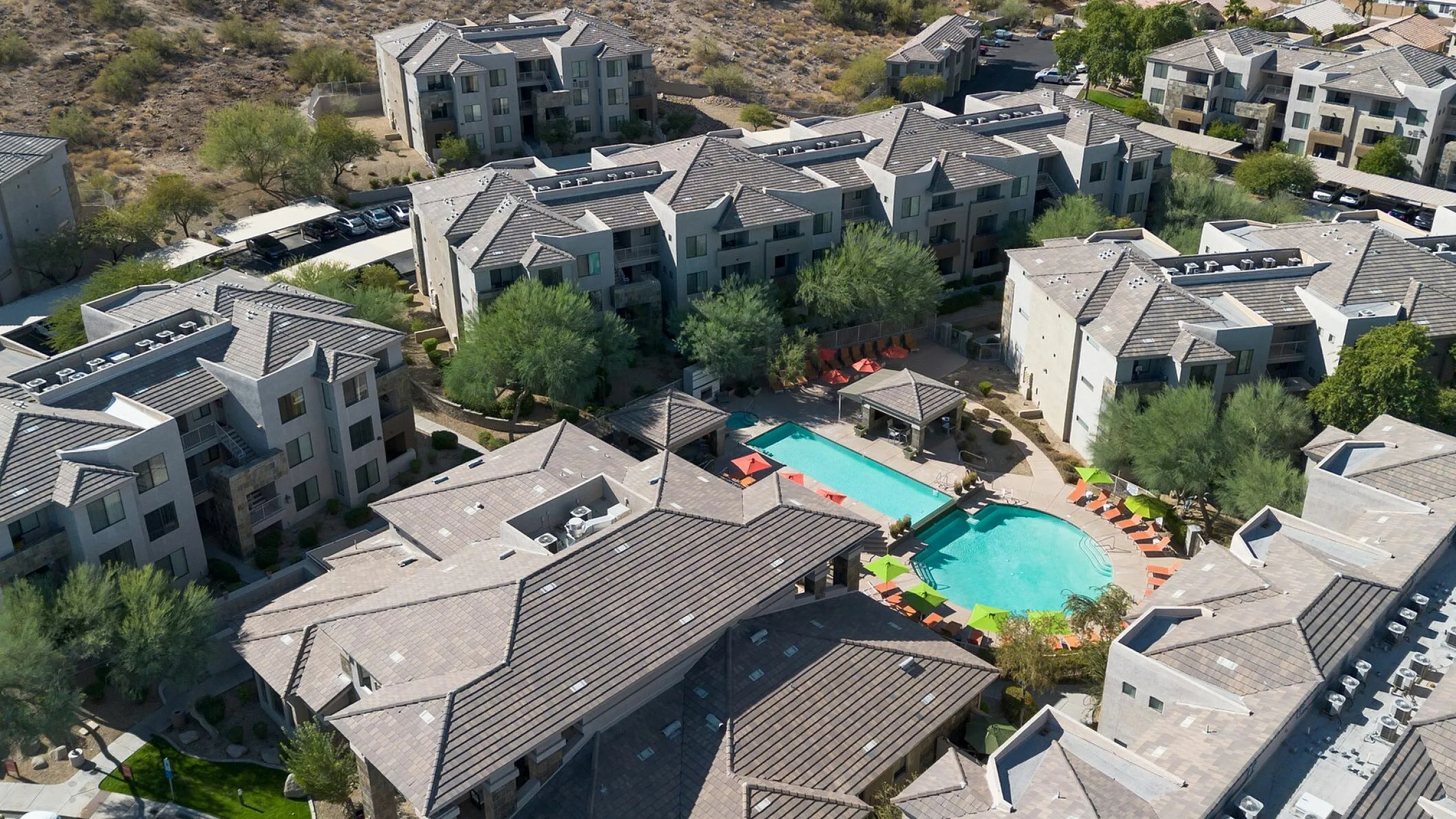 Luxurious apartment complex with stunning mountain views, featuring a sparkling pool surrounded by modern architecture and lush greenery.