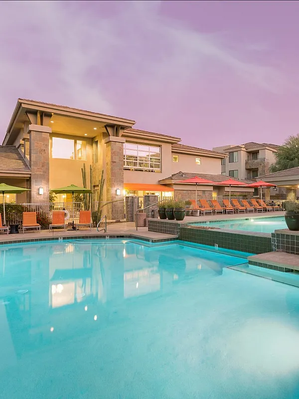 Luxurious apartment complex with a stunning pool area, surrounded by modern architecture and vibrant outdoor seating under a twilight sky.