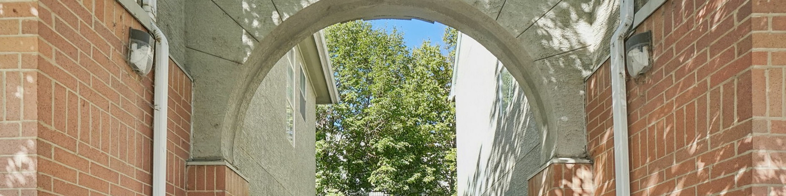 Inviting pathway with brick archway leading to lush greenery and modern staircase, ideal for welcoming apartment entrance.