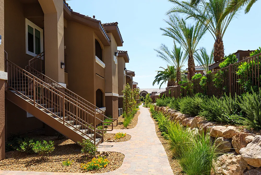 Charming apartment complex with palm-lined pathways, manicured greenery, and elegant exterior staircases leading to stylish units.