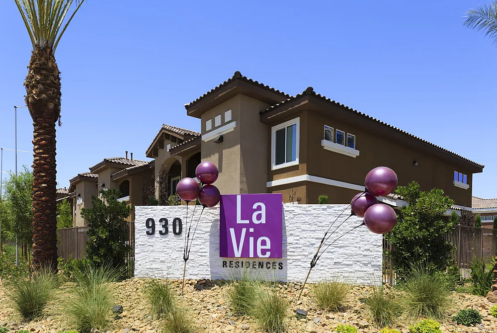 Sunny exterior view of La Vie Residences showcasing modern architecture with a welcoming sign and vibrant landscaping.