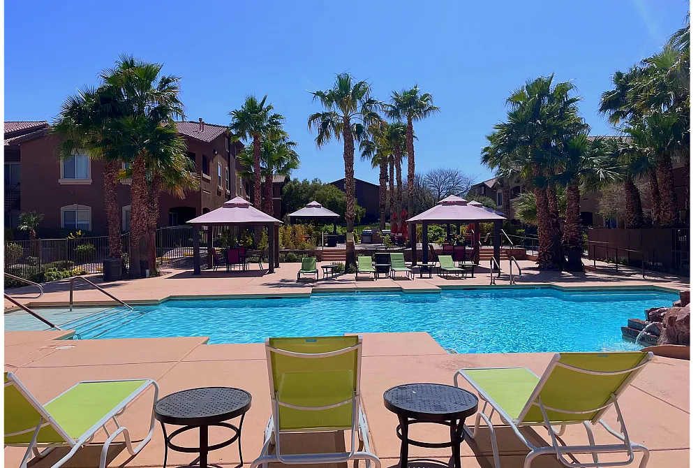 Serene apartment pool area with inviting lounge chairs, tropical palm trees, and shaded seating, perfect for relaxation and leisure.