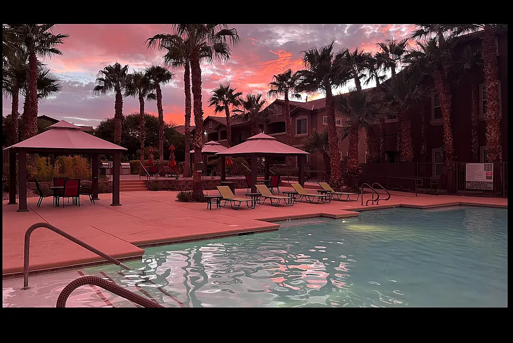 Luxurious apartment complex with stunning poolside view, palm trees, and vibrant sunset skies.