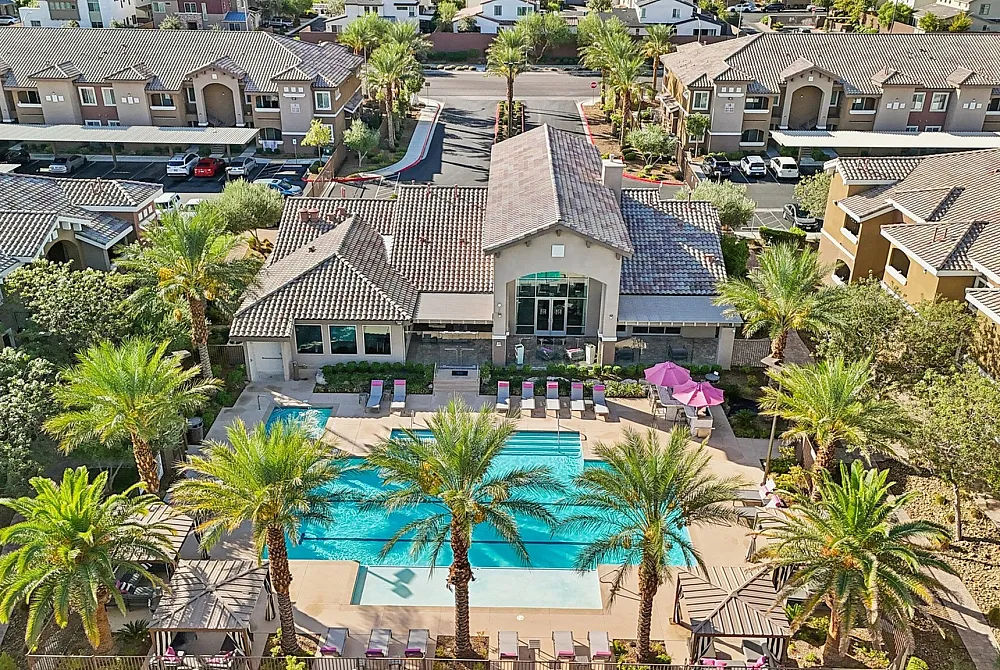 Luxurious aerial view of a stylish apartment complex with a sparkling swimming pool surrounded by palm trees and elegant architecture.