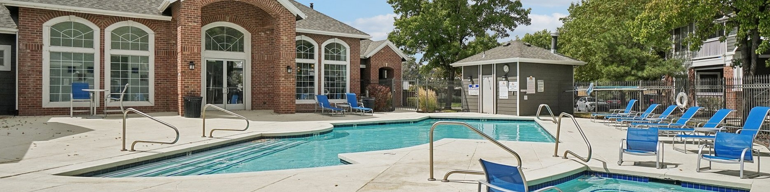 Inviting apartment community pool area with comfortable lounge chairs and vibrant greenery under a clear blue sky.