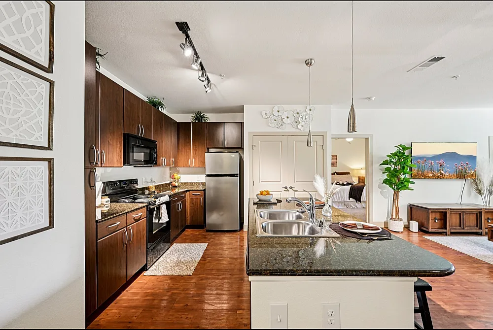 Elegant open-plan kitchen and living area featuring sleek wooden cabinets, granite countertops, and modern appliances, leading to a cozy bedroom.