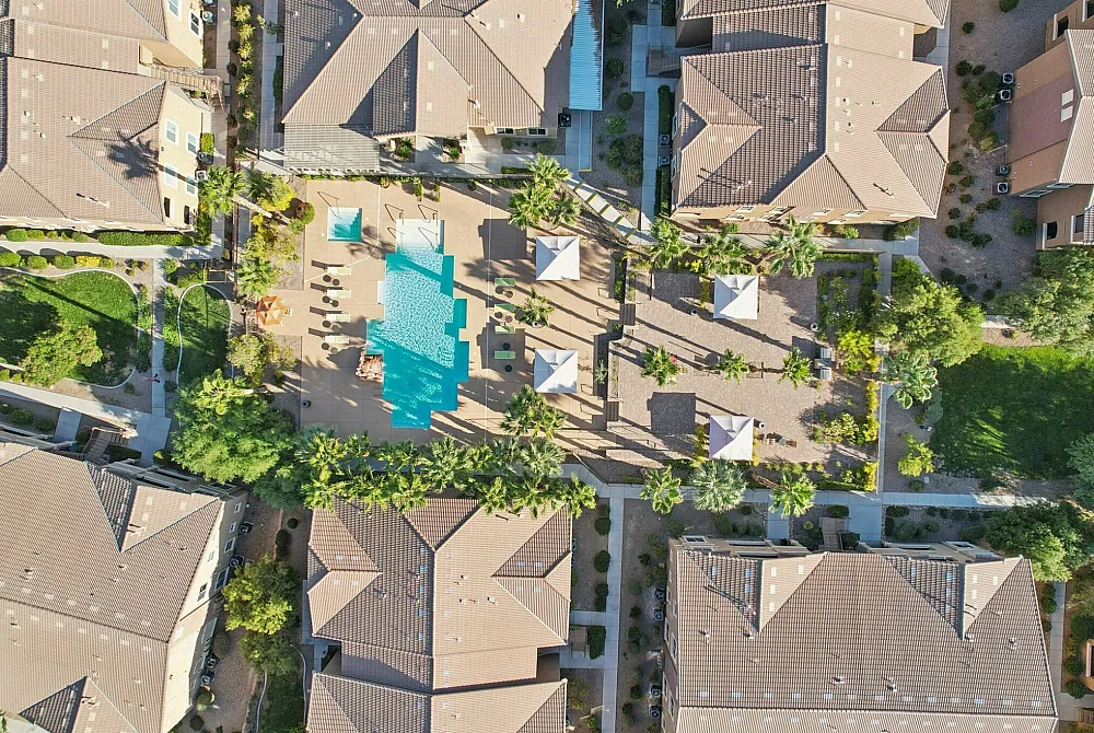 Aerial view of an upscale apartment complex with a sparkling pool, lush greenery, and elegant patio areas, perfect for relaxation and leisure.