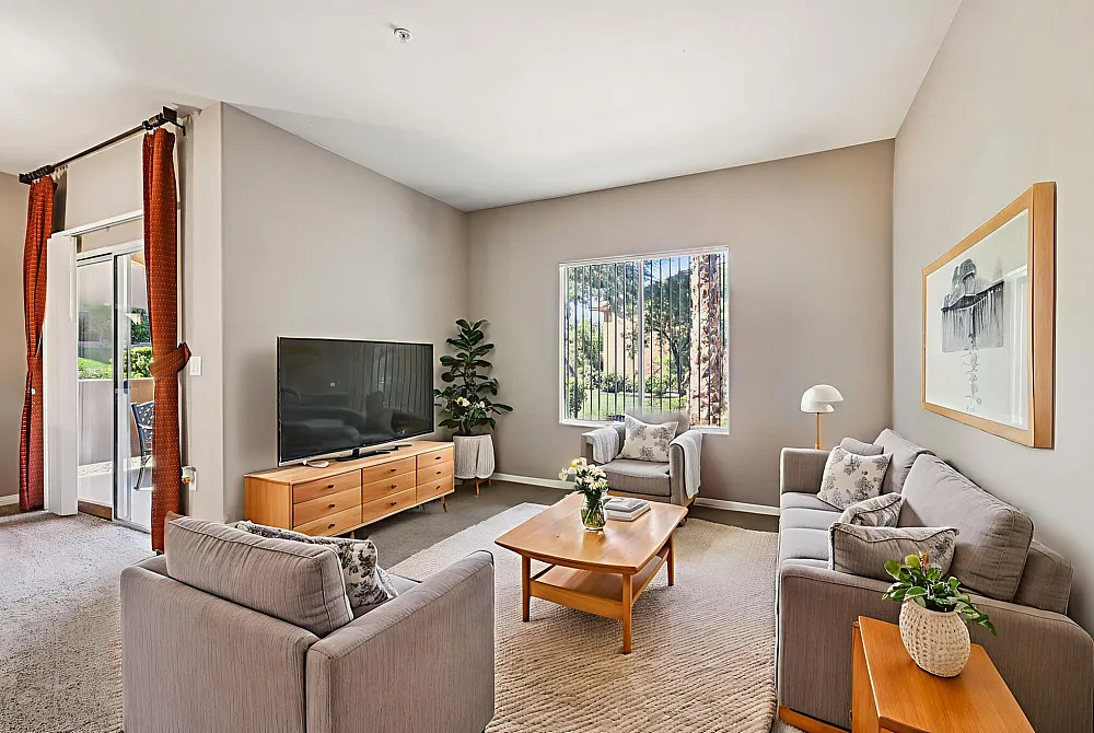Bright and inviting living room with modern furniture, large TV, and a view of lush greenery through the window.