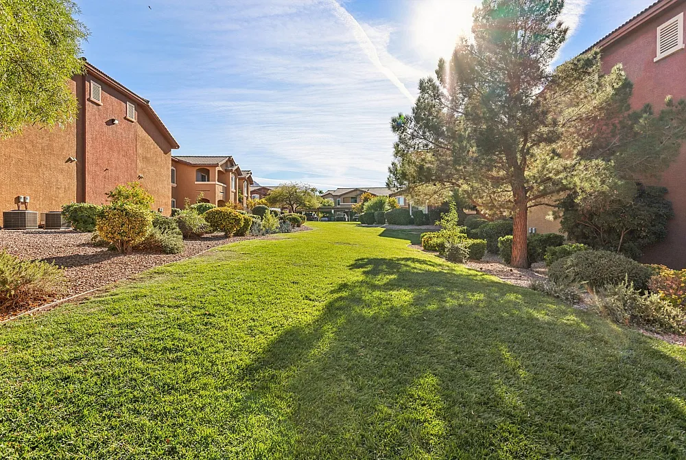 Inviting apartment landscape with lush green lawns, vibrant bushes, and towering trees under a bright blue sky.