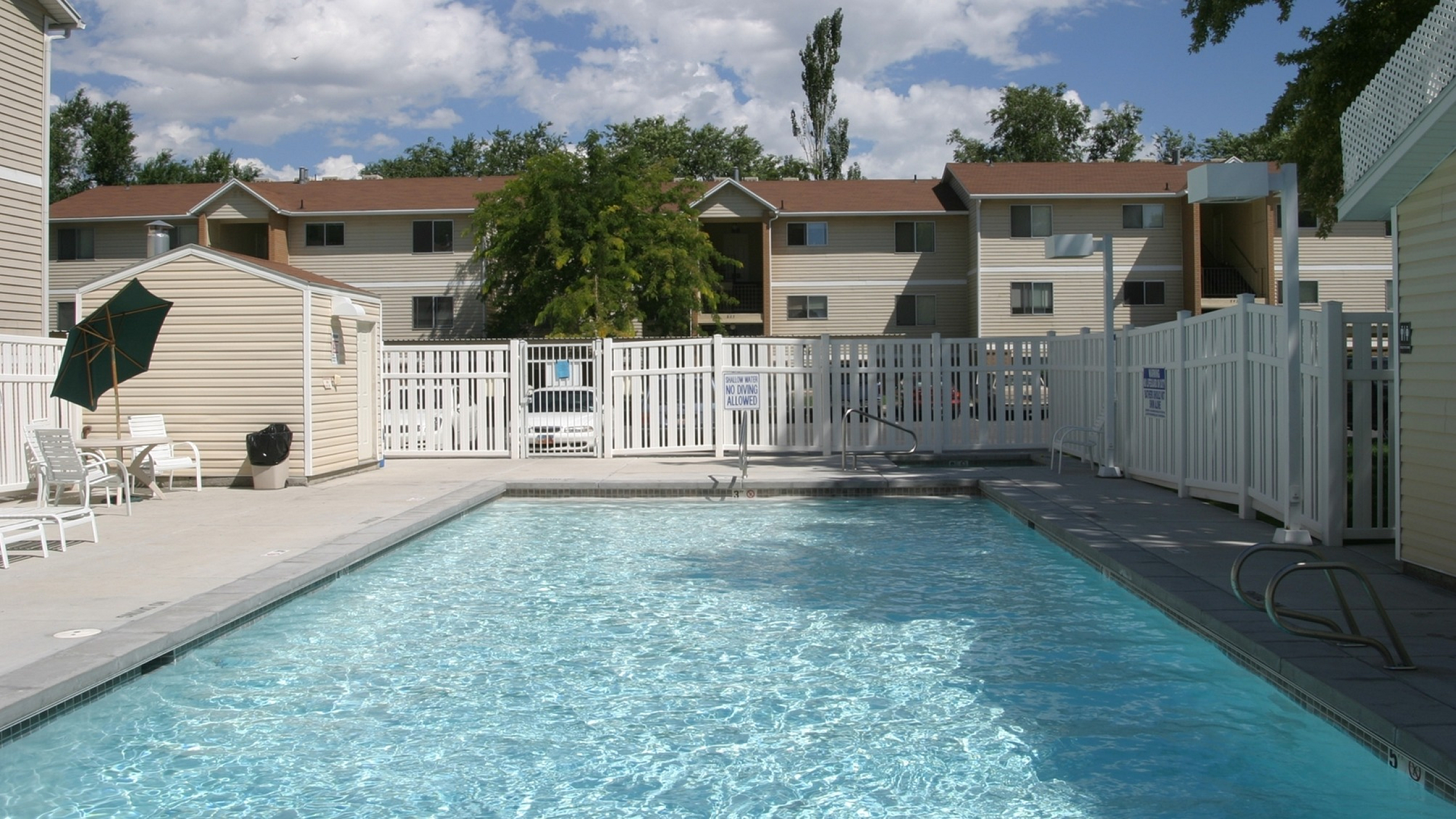 Charming apartment complex featuring a sparkling pool with lounge chairs and umbrellas, perfect for sunny relaxation.