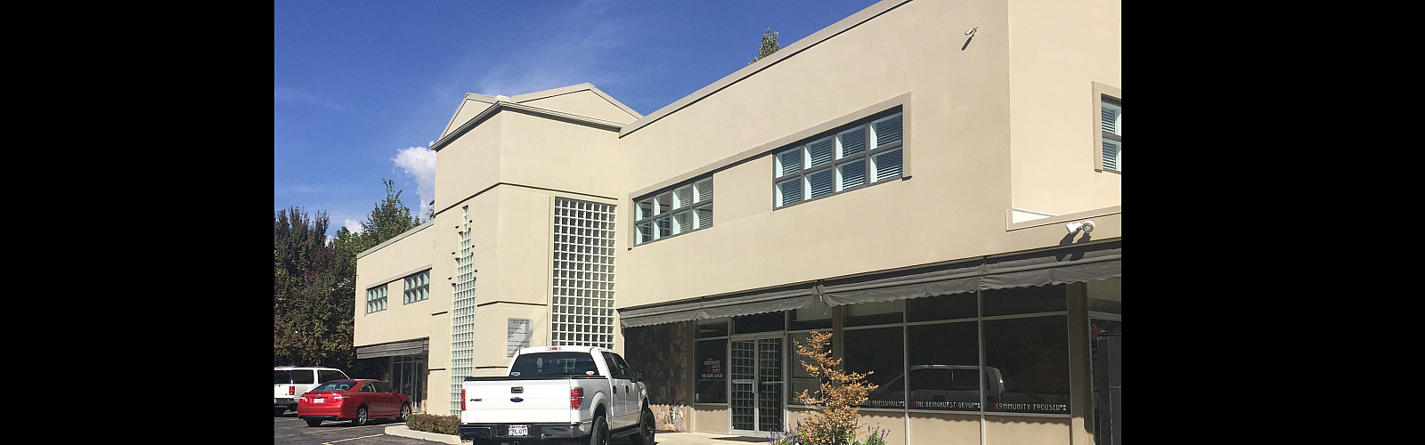 Modern commercial building with sleek architecture, large windows, and ample parking space under a bright blue sky.