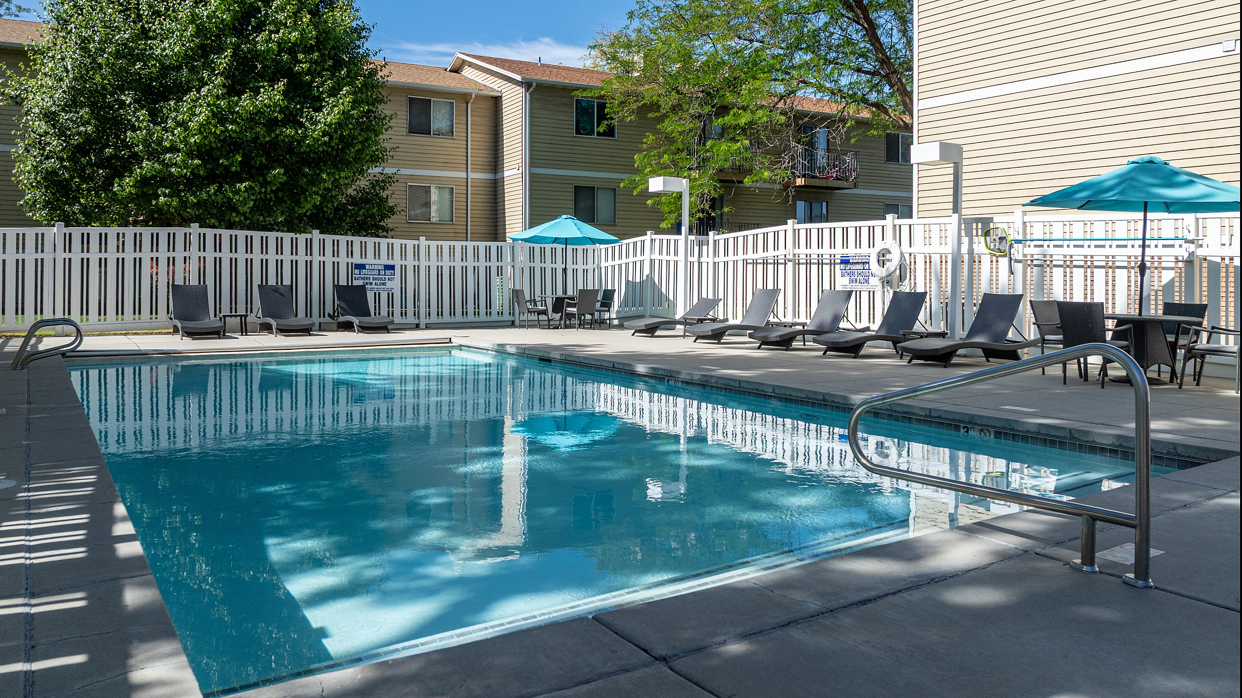 Inviting apartment complex pool area with comfortable lounge chairs, umbrellas, and lush greenery for a perfect relaxation spot.