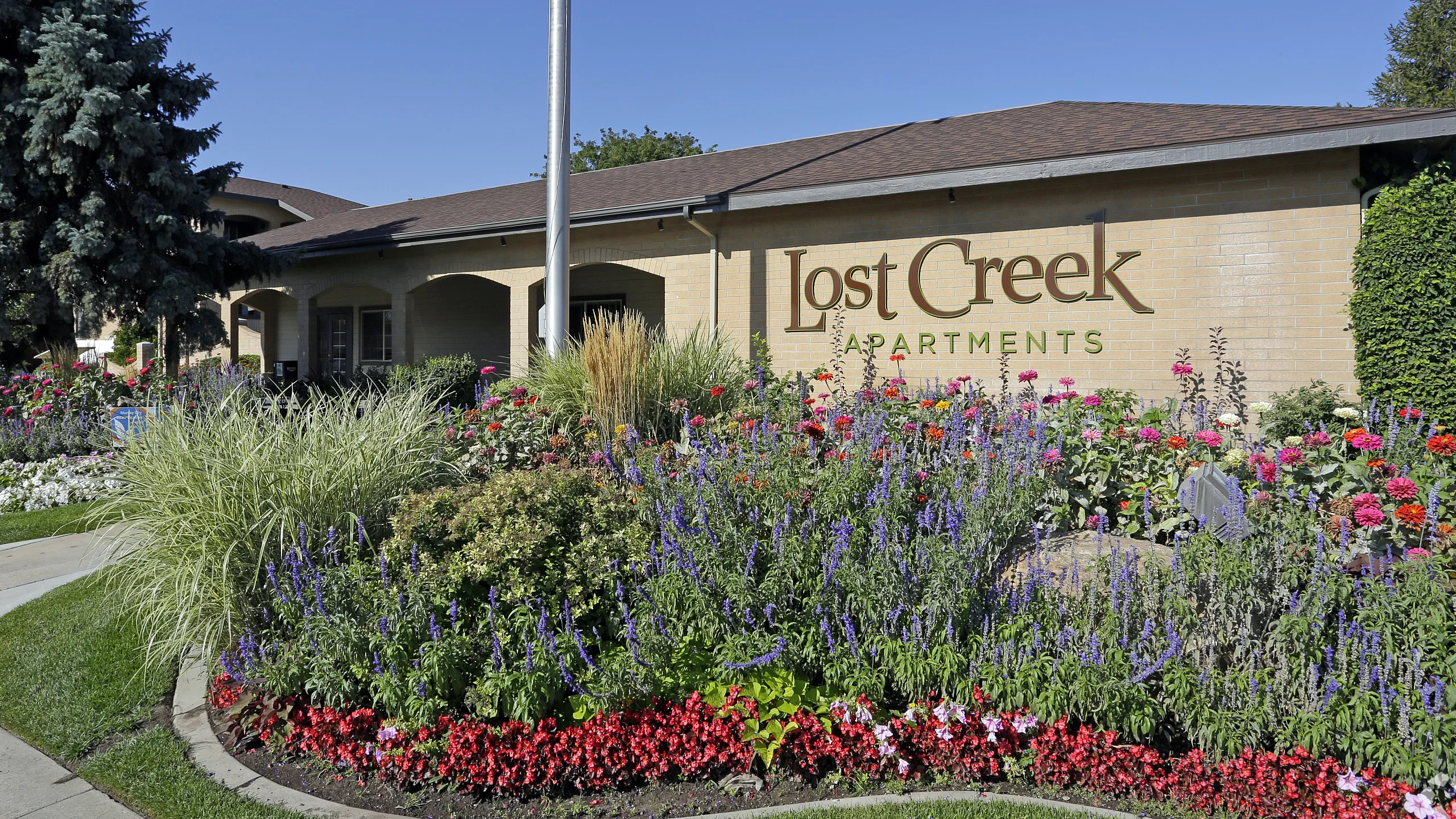 Charming exterior of Lost Creek Apartments showcasing vibrant flower beds and lush greenery under a clear blue sky.