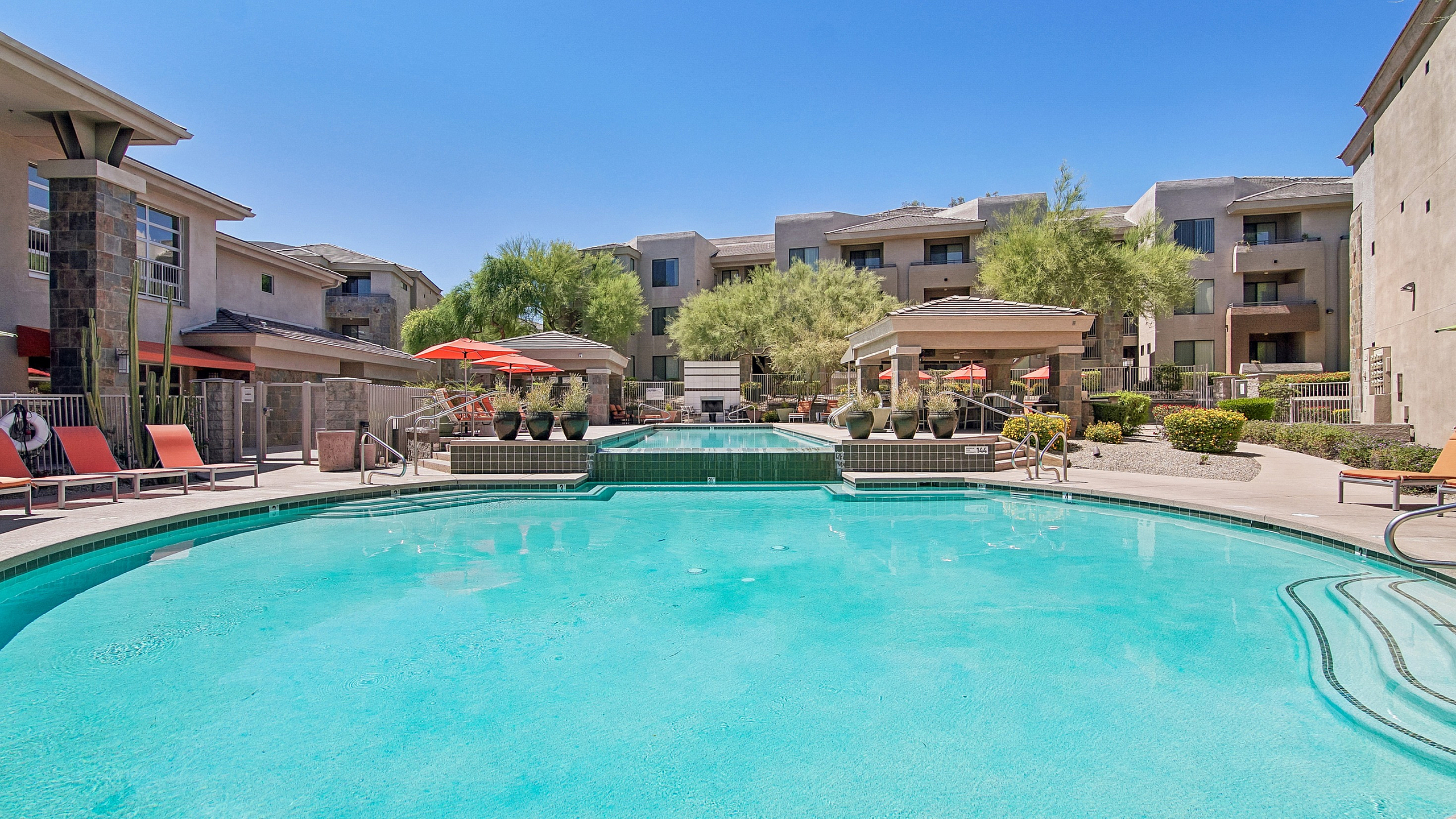 Sparkling pool, lush landscaping, and shaded loungers under vibrant umbrellas.