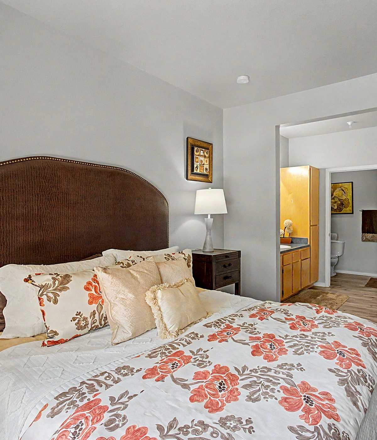 Inviting bedroom with floral bedding, elegant dark wood furniture, and a cozy ambiance leading to a stylish en-suite bathroom.