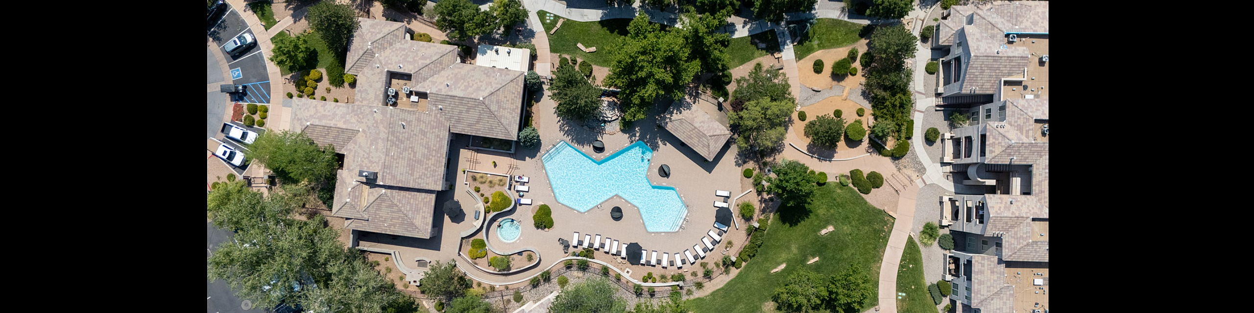 Aerial view of a luxurious apartment complex showcasing a large, uniquely shaped swimming pool, surrounded by lush greenery and modern architecture.