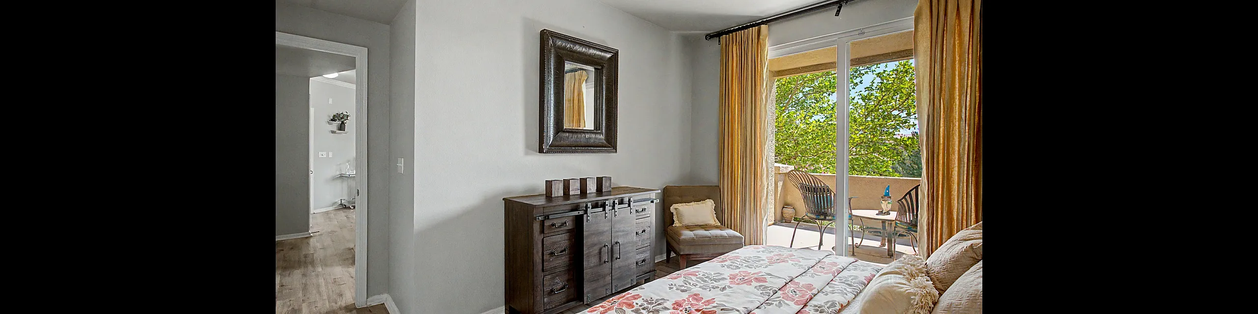 Bright and inviting bedroom featuring floral bedding, elegant drapes, and access to a cozy balcony with lush greenery views.
