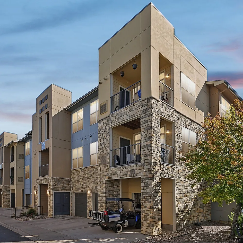 Contemporary multi-story apartment building with stone accents and balconies, set against a beautiful sky, offering modern urban living.