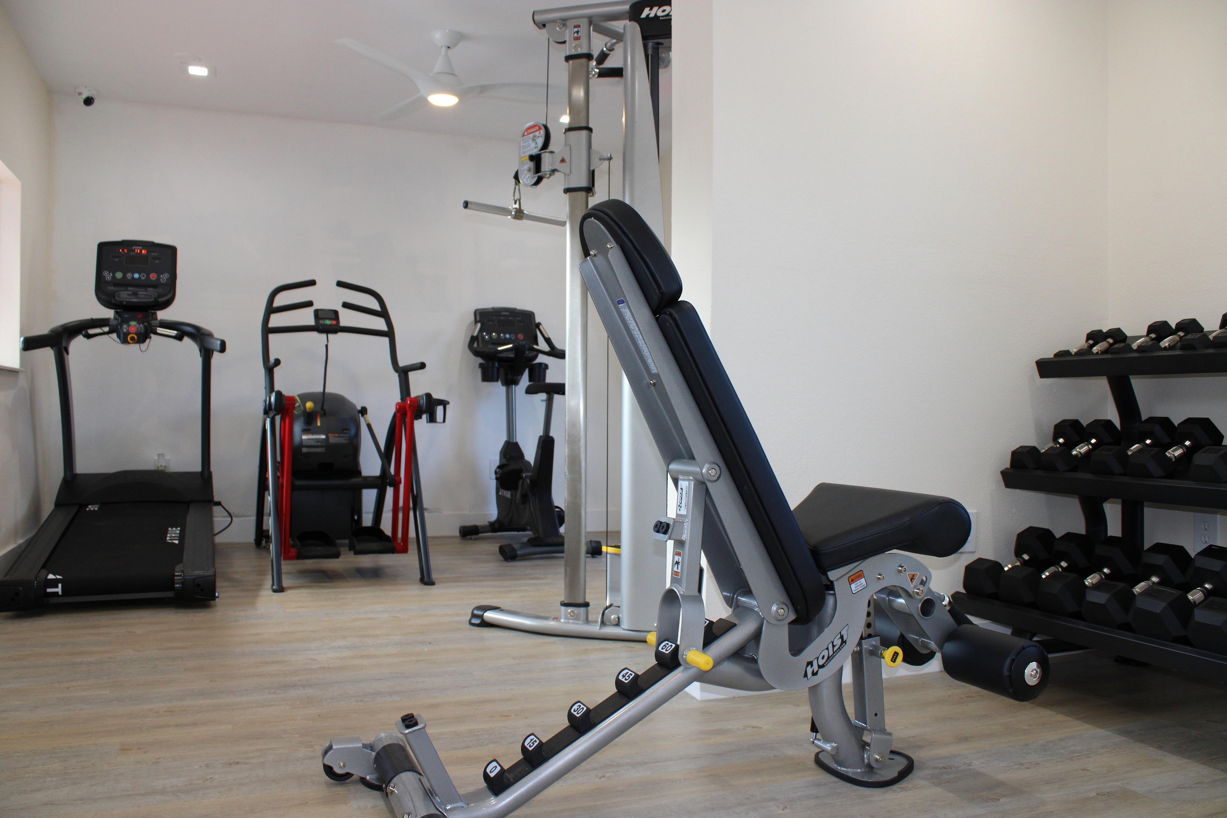 Modern apartment fitness room equipped with treadmill, elliptical, multi-gym station, and a rack of sleek dumbbells.