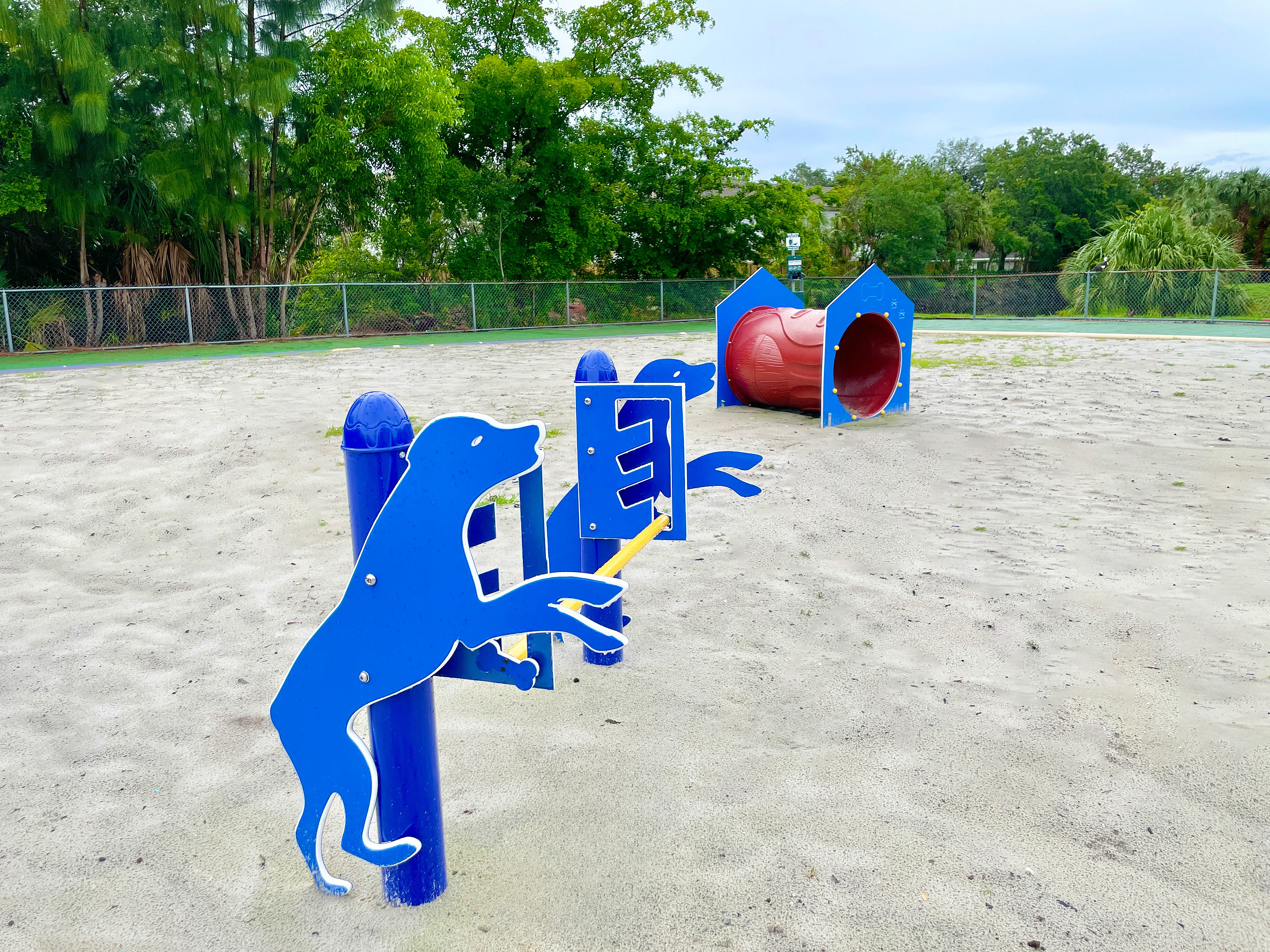 Charming playground with vibrant blue dog-themed agility station and a red tunnel slide set amidst lush greenery.