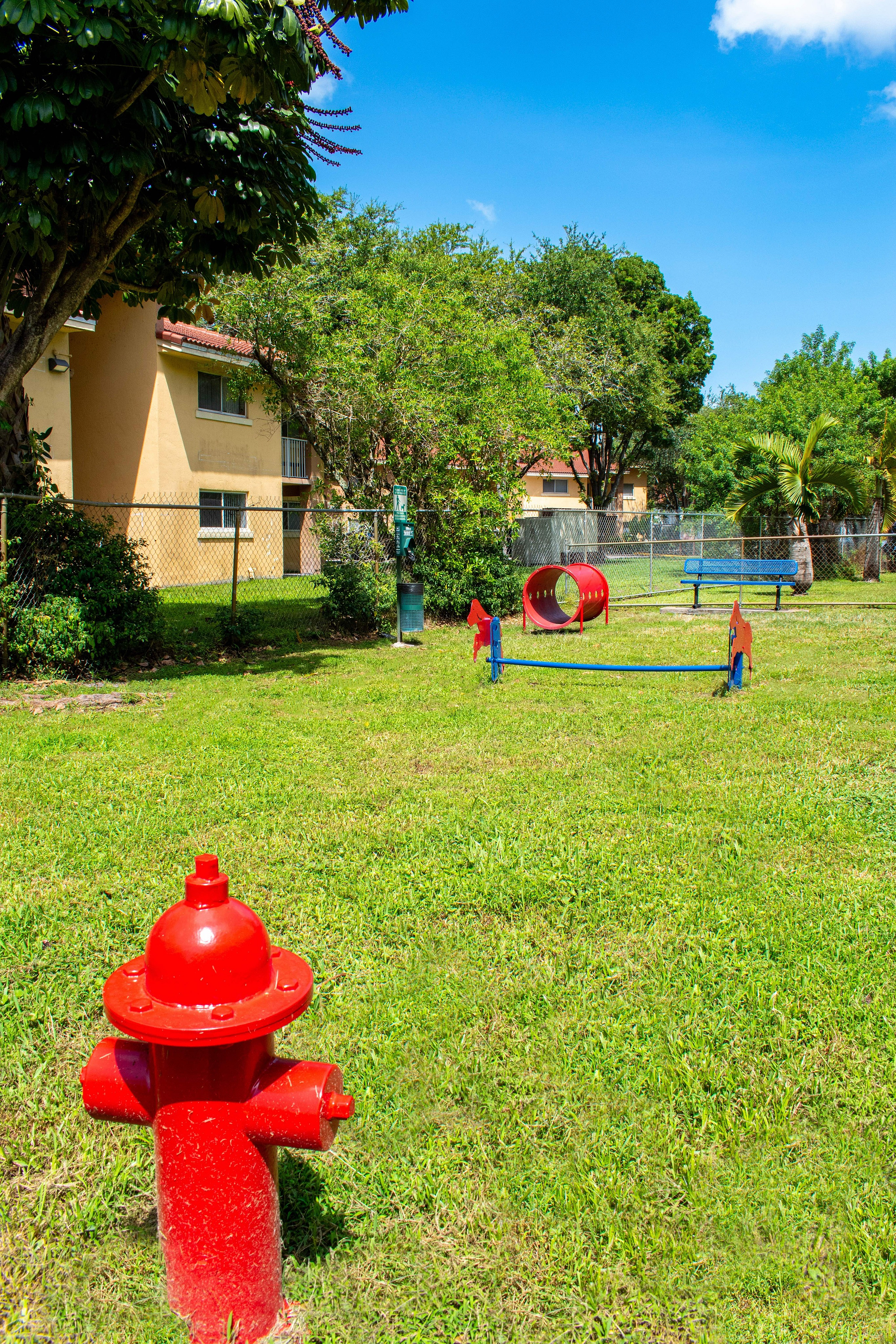 Charming apartment courtyard with vibrant playground, lush greenery, and bright red fire hydrant under a clear blue sky.
