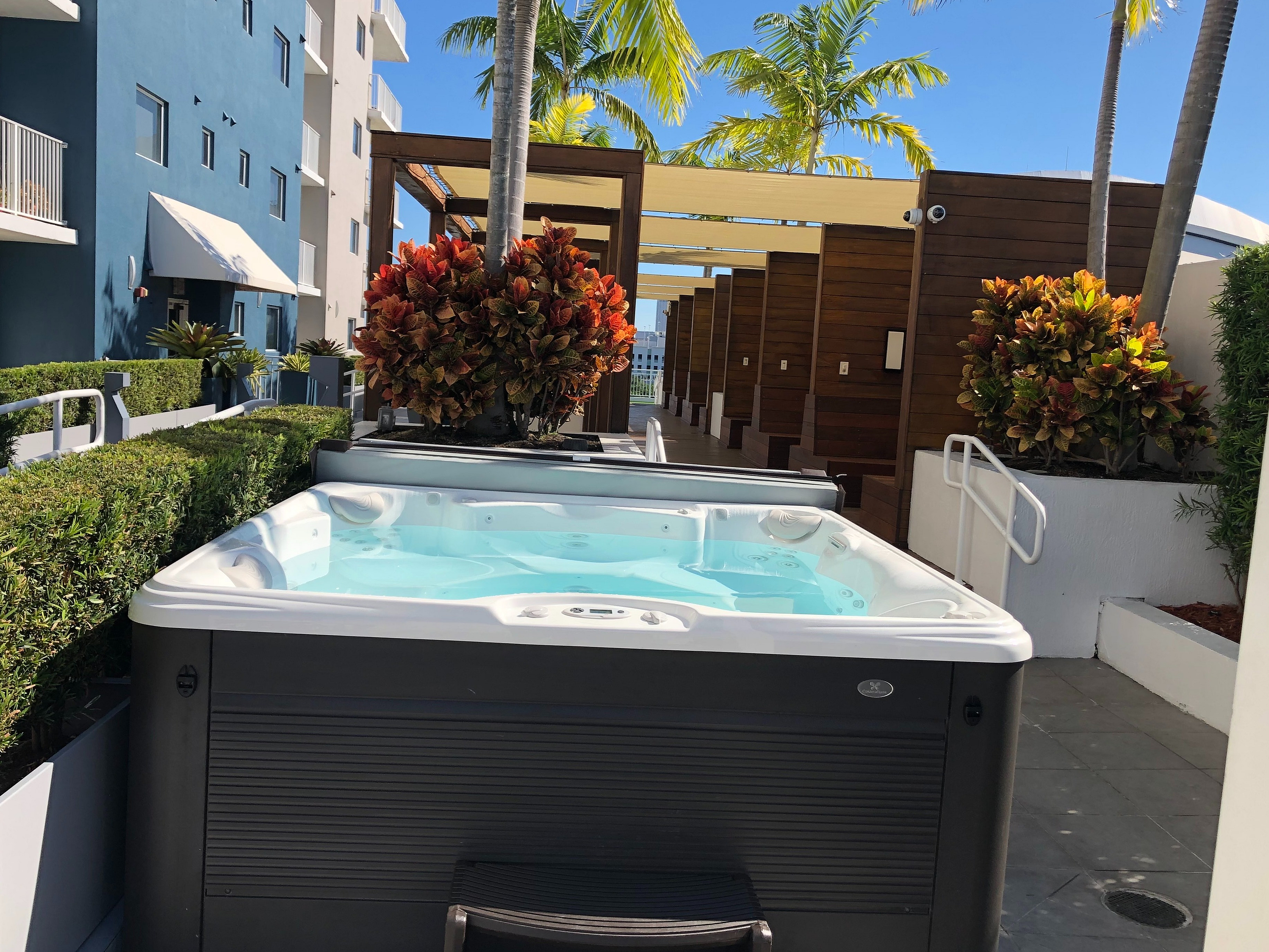 Luxurious outdoor area in a modern apartment complex featuring a sleek hot tub, vibrant landscaping, and stylish cabanas under palm trees.