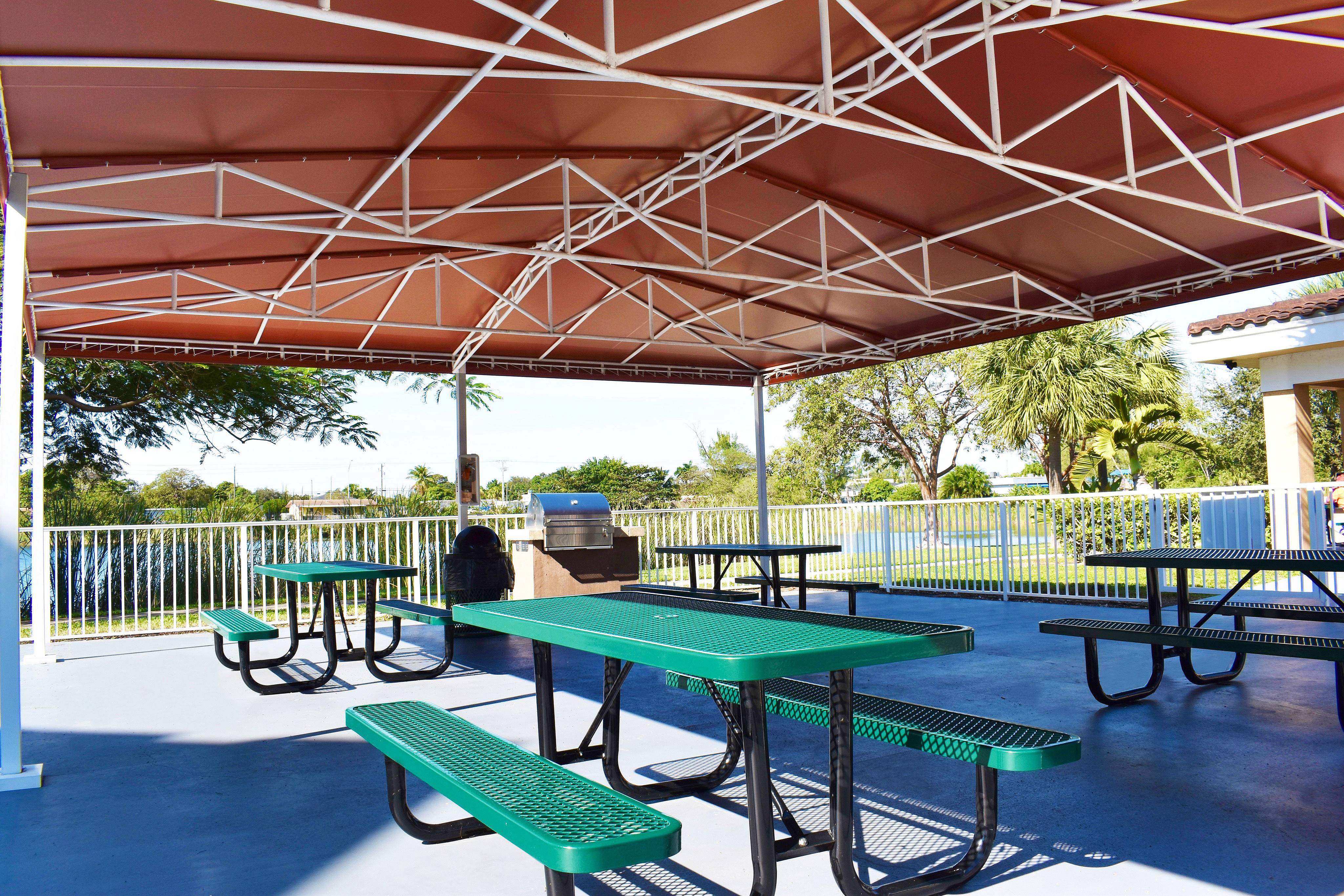 Inviting outdoor pavilion with green picnic tables, perfect for relaxing under a stylish gazebo surrounded by lush greenery.